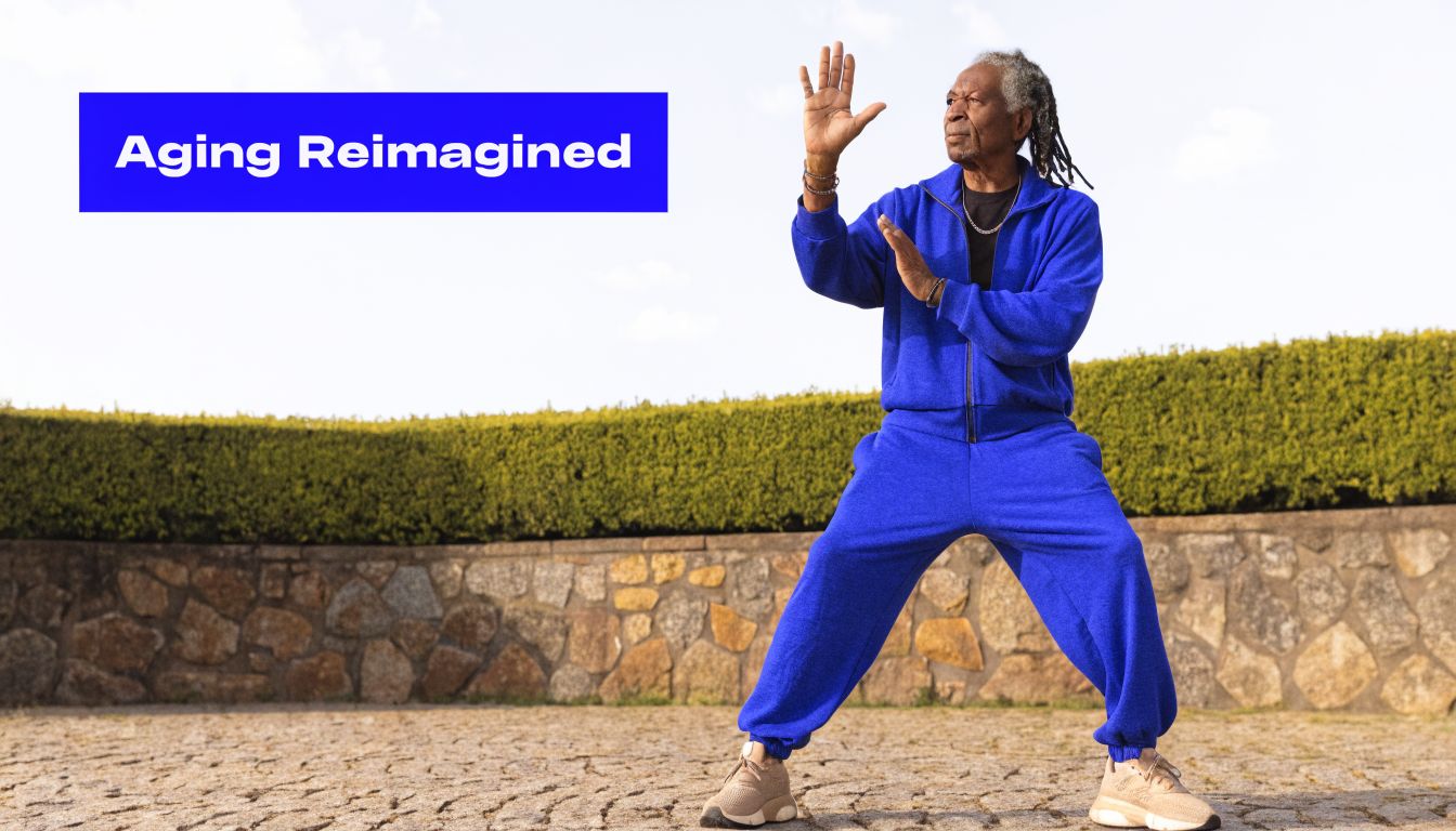 A fit senior man with dreadlocks wearing a blue tracksuit practicing tai chi outdoors at sunrise.