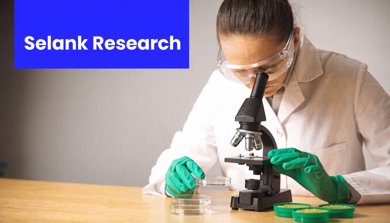 A scientist in a lab coat and green gloves using a microscope to study samples.