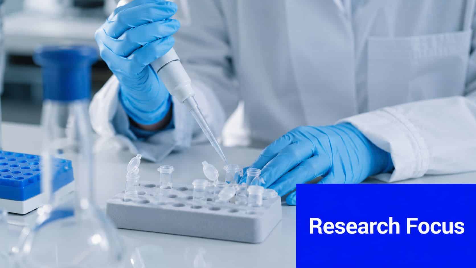 A laboratory scientist in protective gear using a pipette to transfer liquid into small test tubes.